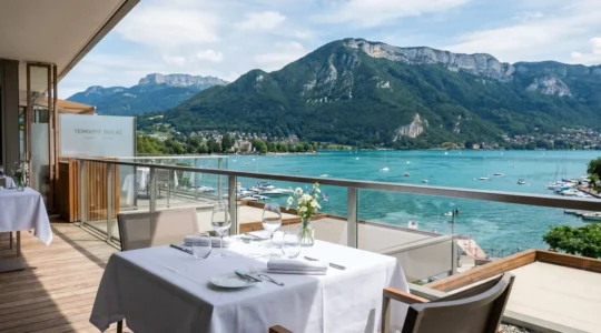 Terrasse élégante face au lac d'Annecy turquoise avec table dressée au premier plan et massif montagneux en arrière-plan sous lumière naturelle